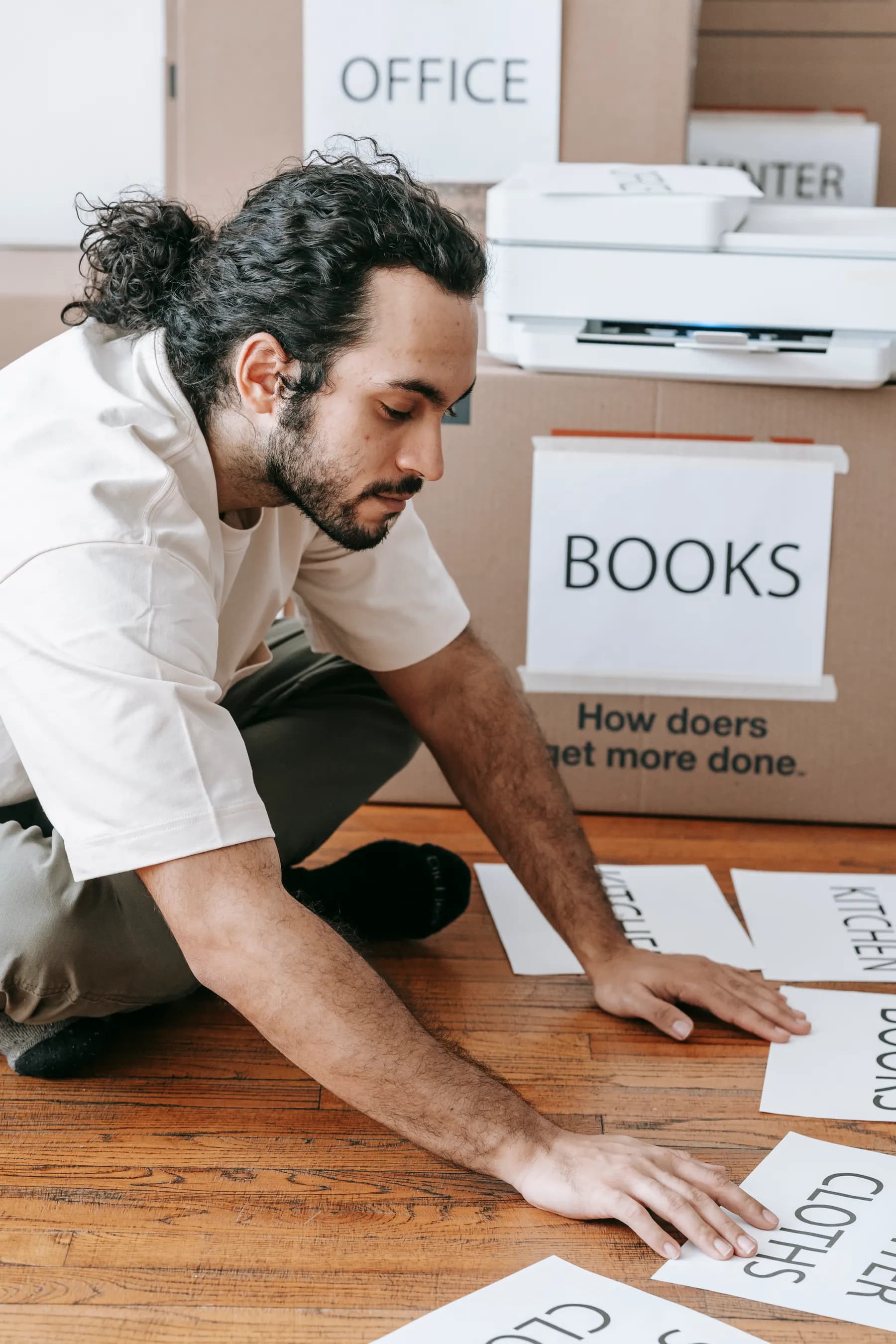 A person sorts printed category names beside labelled moving boxes and a printer.