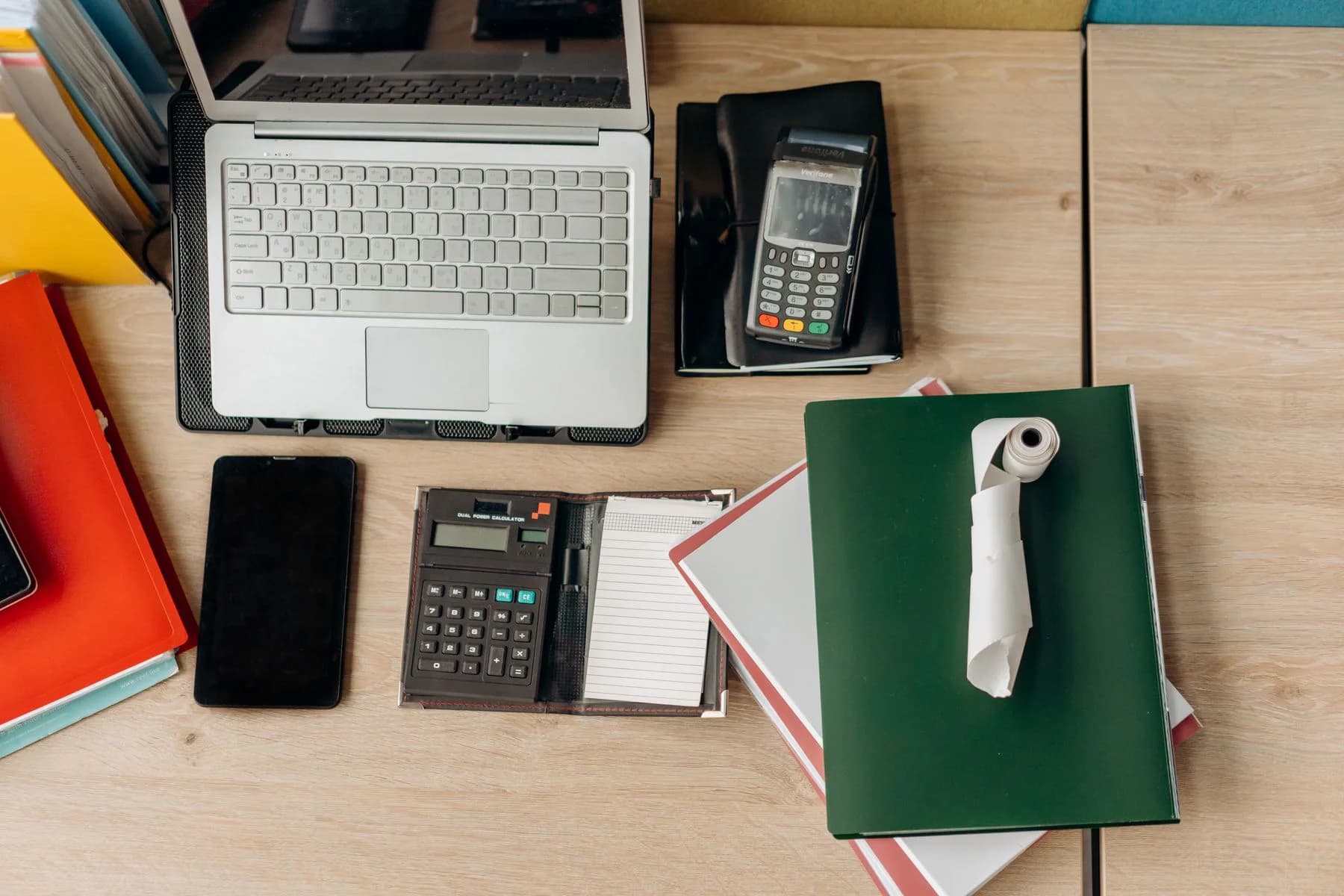 A laptop, smartphone, payment terminal, calculator, and documents on a real office desk