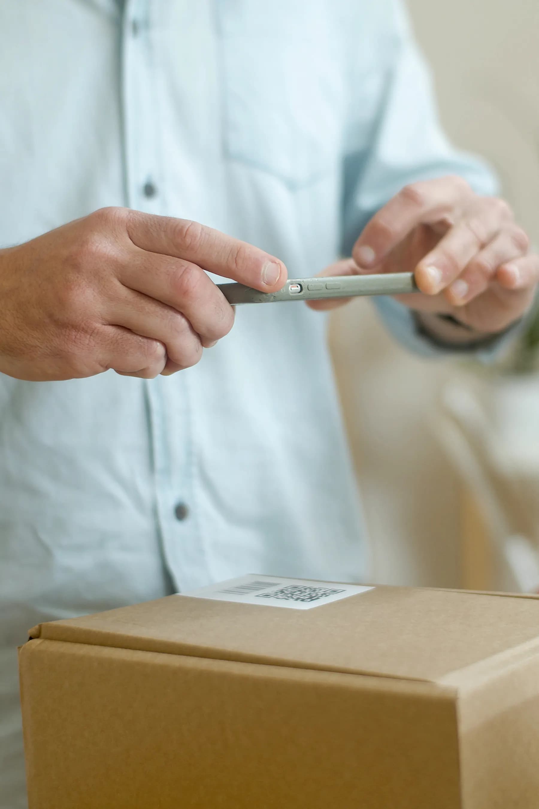 A person holds a smartphone above a QR label on a cardboard box.